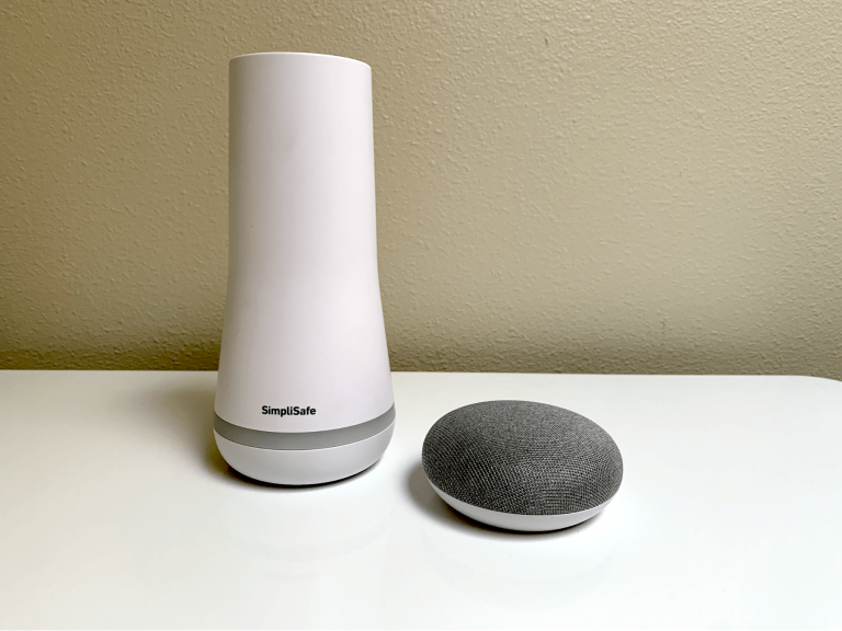 SimpliSafe base station pictured on a white tabletop next to a gray Google Nest Mini speaker