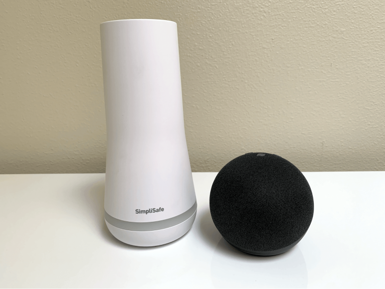White SimpliSafe base station pictured next to a black Amazon Echo Dot on a tabletop