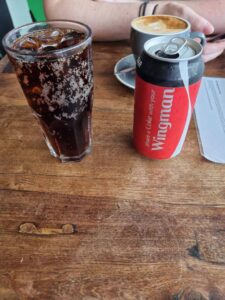 A photo of a Coke can and tall glass of soda on a wooden table