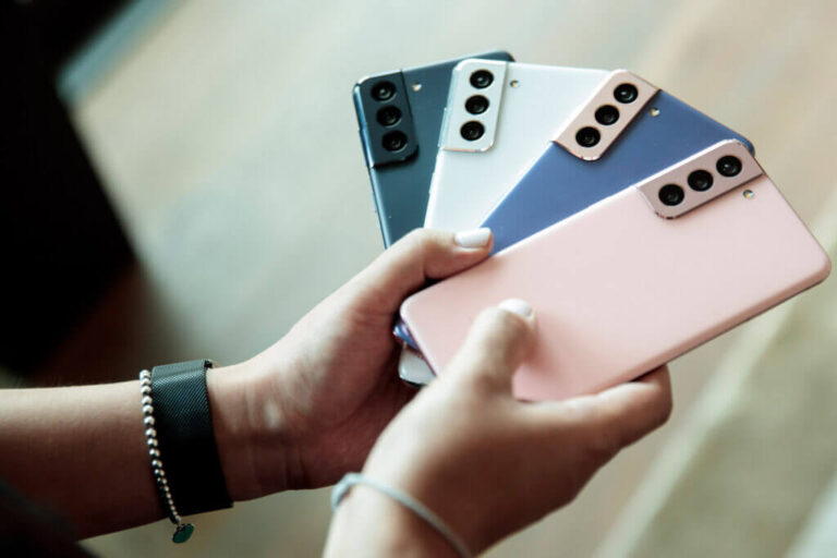 A close up of a woman's hands holding four Samsung Galaxy S21 cell phones in pink, blue, white, and grey