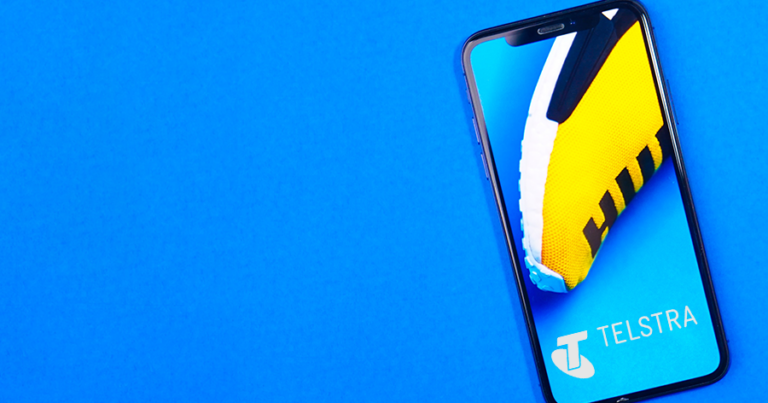 Foto ponsel cerdas dengan logo Telstra di latar belakang biru