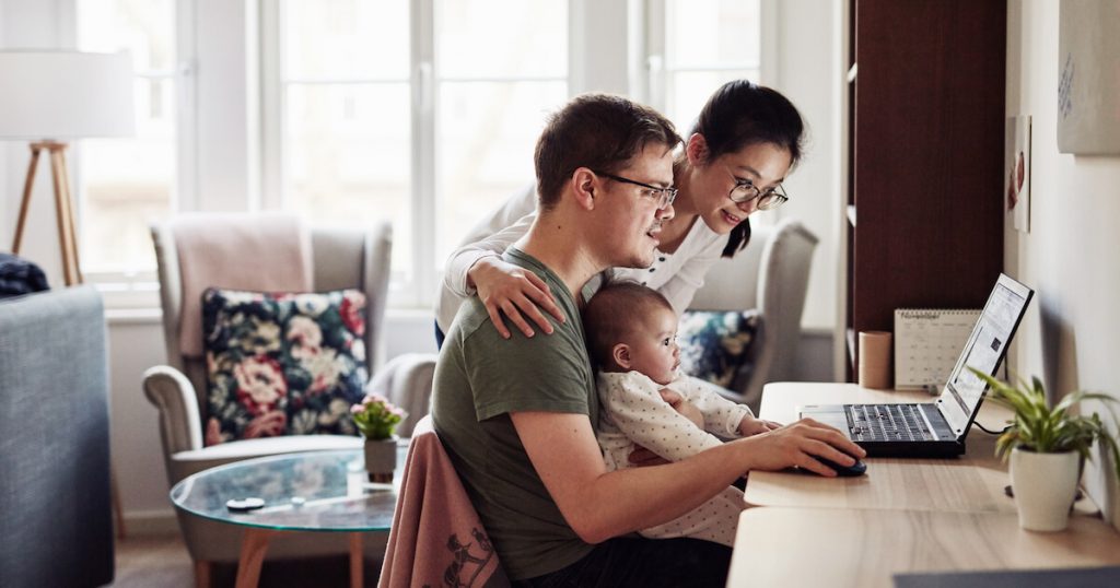 An infant sits in dad's lap while a young couple uses a laptop