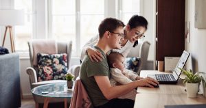 An infant sits in dad's lap while a young couple uses a laptop