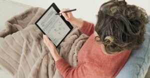Woman lying on a couch, taking notes on a Kobo Elipsa