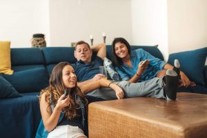 Dad and two daughters lounging on living room couch watching TV
