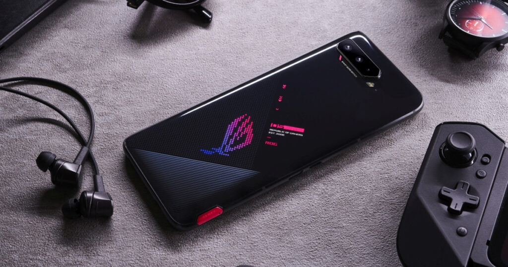 Photograph of the ASUS ROG Phone 5 next to headphoens and a gaming controller