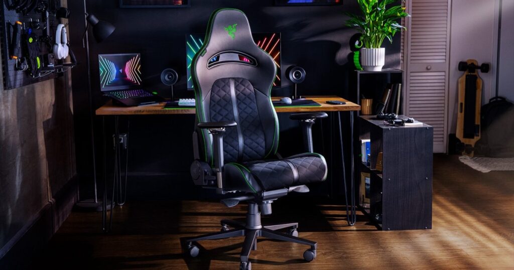 Black Razer Enki gaming chair with green stitching at a desk with a laptop, monitor, keyboard and mouse