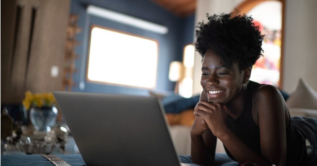 A Black woman smiles as she looks at the screen of her laptop