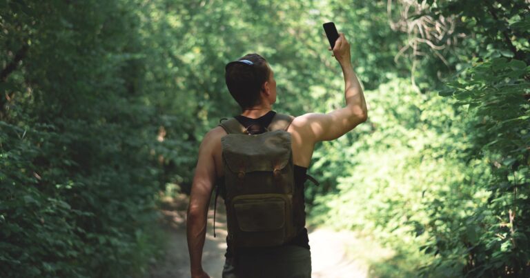 Photograph of a man in on a bushwalk looking for mobile phone coverage