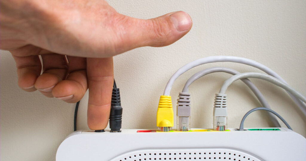 Photograph of a hand pushing the power button on a modem