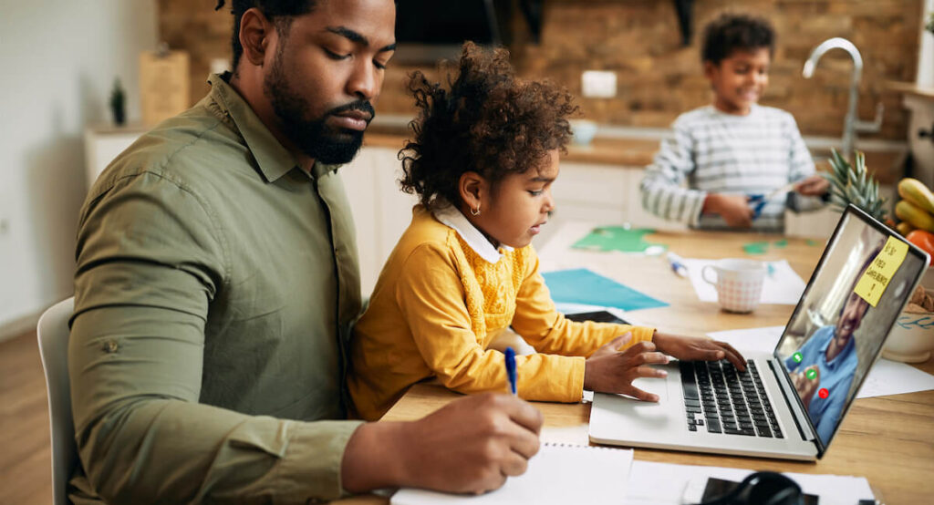 A Black father babysits his two young children while working from home on a laptop