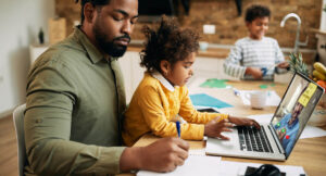 A Black father babysits his two young children while working from home on a laptop