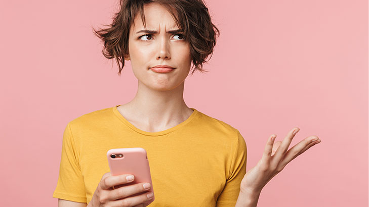 woman in yellow top holding phone looking confused