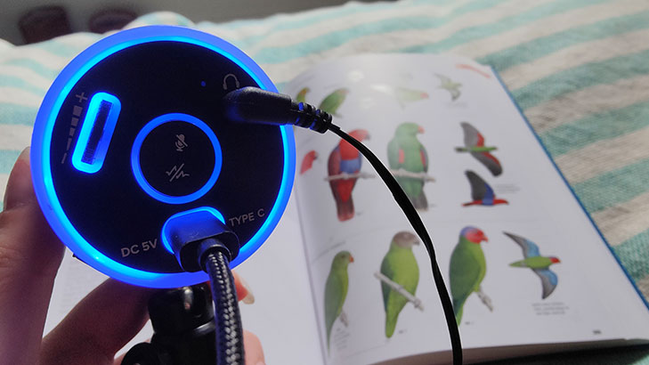 Thronmax Pulse microphone lit up blue with a bird book in background