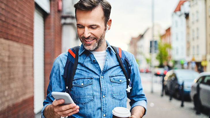 man in denim jacket holding phone and coffee