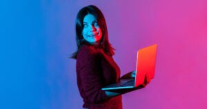 Stylised photo of woman using laptop with pink and blue lighting