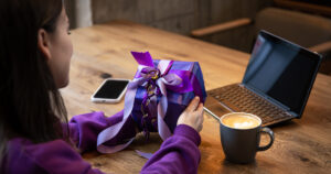 Photograph of a woman opening a purple gift while using her mobile phone and internet