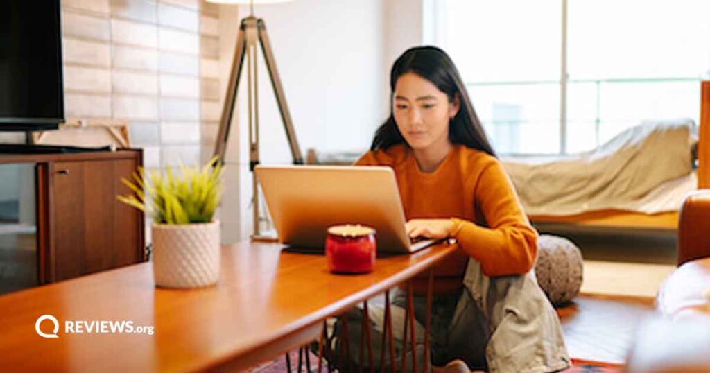 An Asian woman sits at a wooden table with her laptop