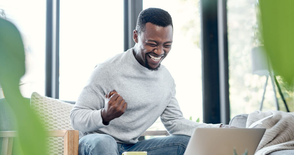 Man is looking at his laptop and is pumping his fist in excitement
