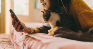 woman staring at charging cell phone while holding a cat