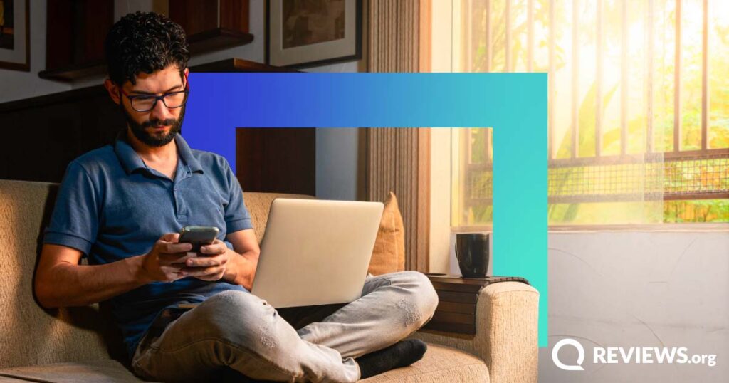 Man uses laptop and cellphone while sitting on a couch