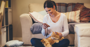 woman smiling at phone with a cat in her lap