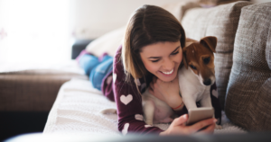 woman smiling at cell phone cuddling dog on a couch