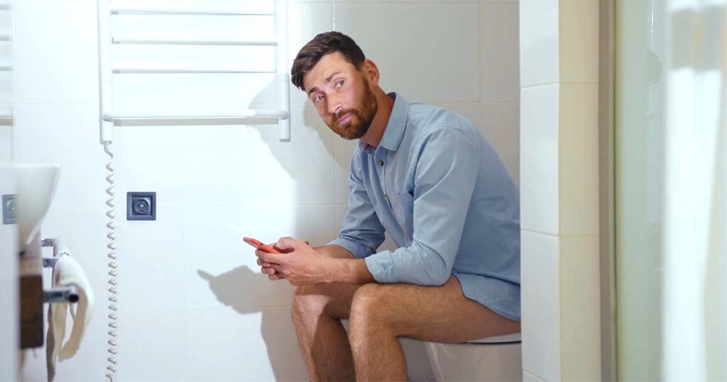 Man using smartphone in bathroom, waiting for phone internet to load