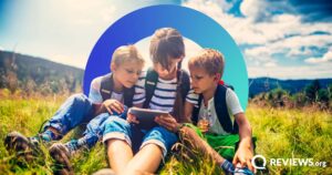 three kids sitting in grass using an ipad with illustration in background