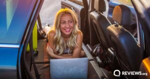 smiling woman using laptop in the back of sedan