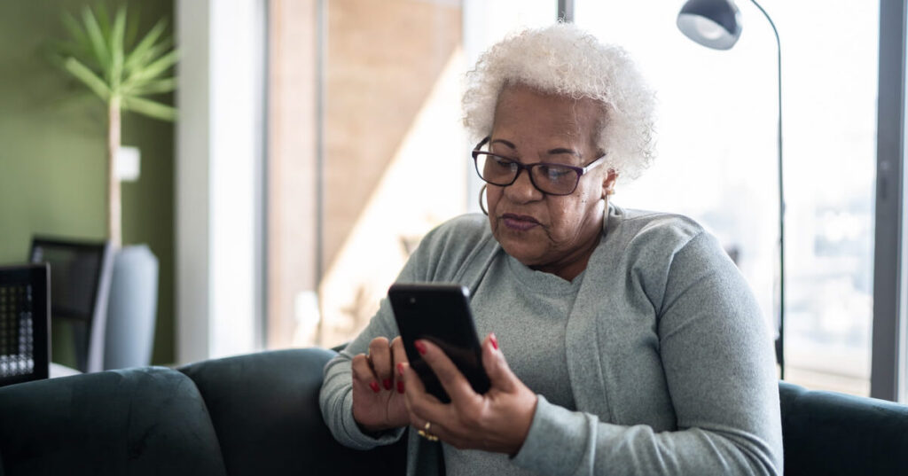 An older woman sits on a couch and uses her phone