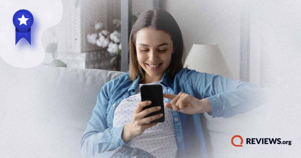 woman using cell phone while sitting on couch and smiling