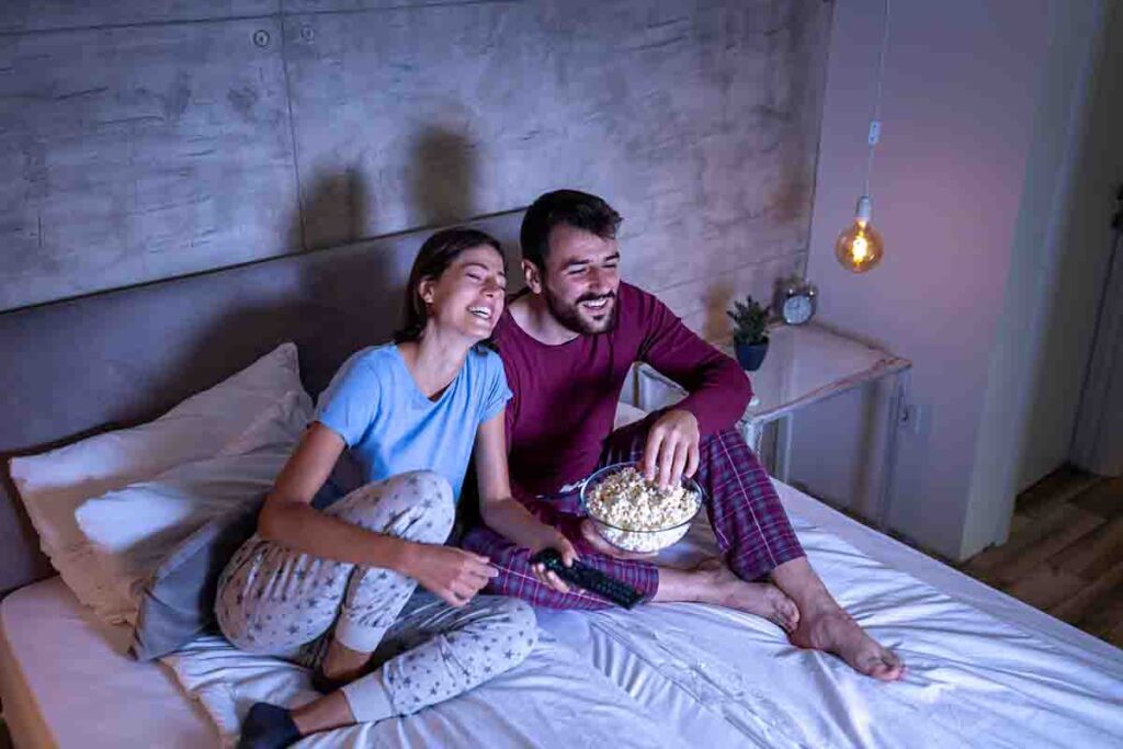 Couple watching streaming service on bed while snacking on popcorn