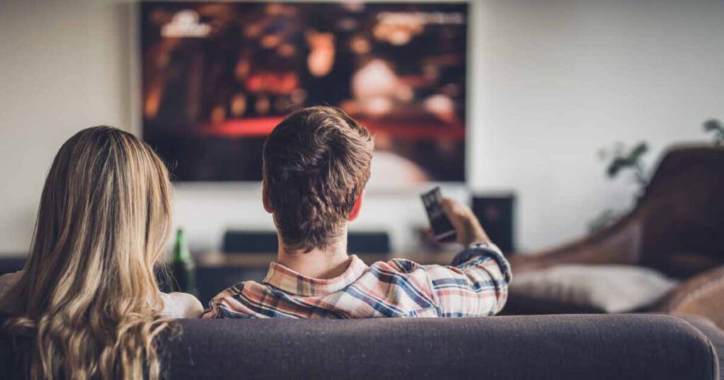 A young couple sitting on the couch in living room watching TV