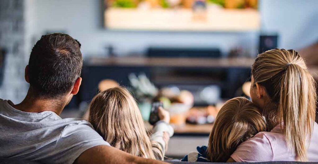 Mom, dad, daughter, and son watching TV on living room couch