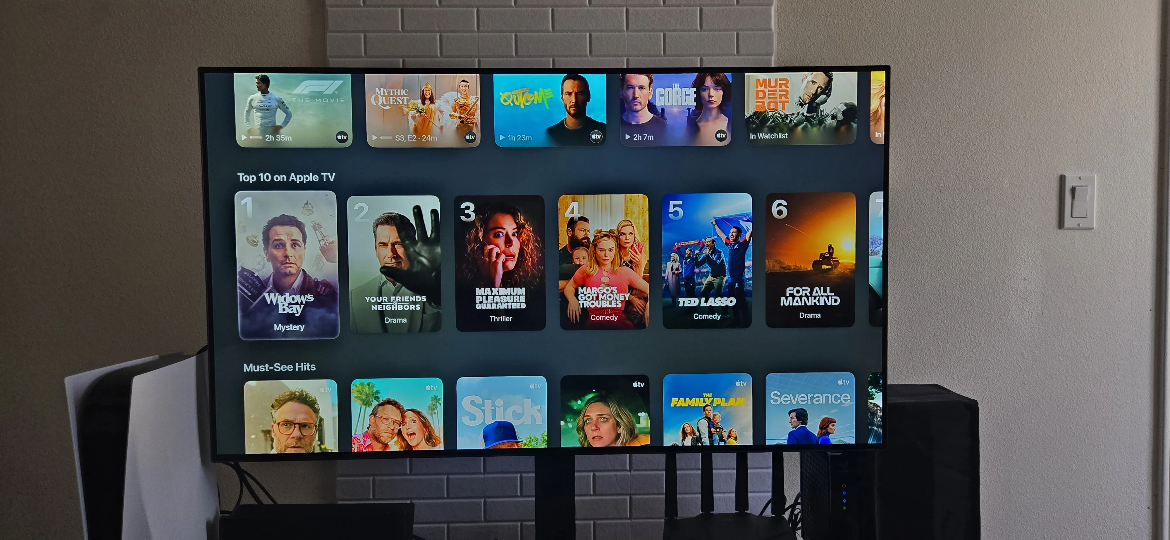 The Apple TV streaming homepage contains rows of titles. On screen there is the Top 10 on Apple TV along with the Must-See Hits.