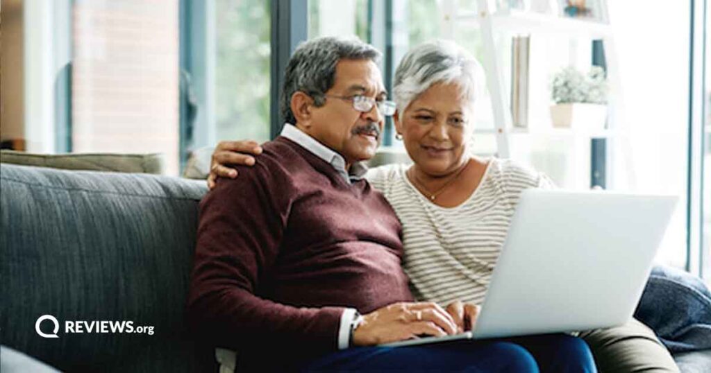 A mature couple sits on a couch looking at a laptop together