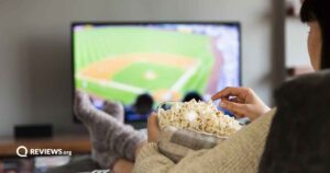 Woman watching baseball on couch while eating popcorn