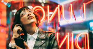 Graphic of a woman using international roaming on her phone in front of a red neon sign