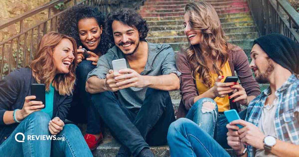 group of people sitting on an outdoor staircase using cell phones looking happy