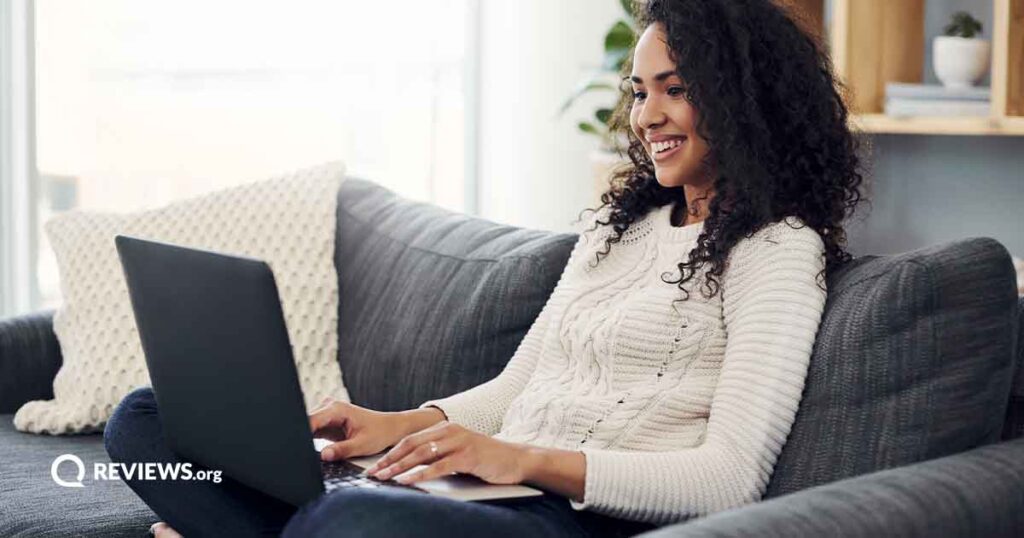 happy woman with curly hair sitting on couch using laptop
