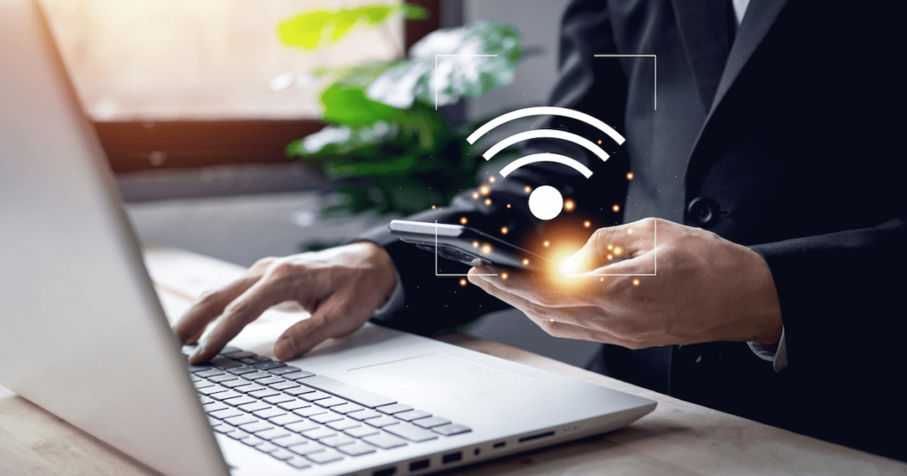 a man in a suit at a laptop activating his wifi hotspot on his phone