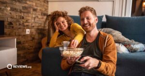 Man and woman sitting on couch with a bowl of popcorn watching tv using a remote