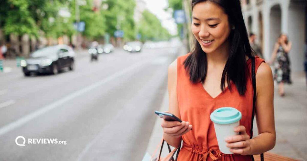Woman holding a cup of coffee and her smartphone next to a city street