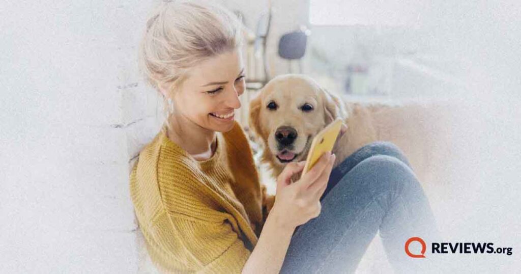 Happy woman sitting on floor using cell phone with a dog next to her