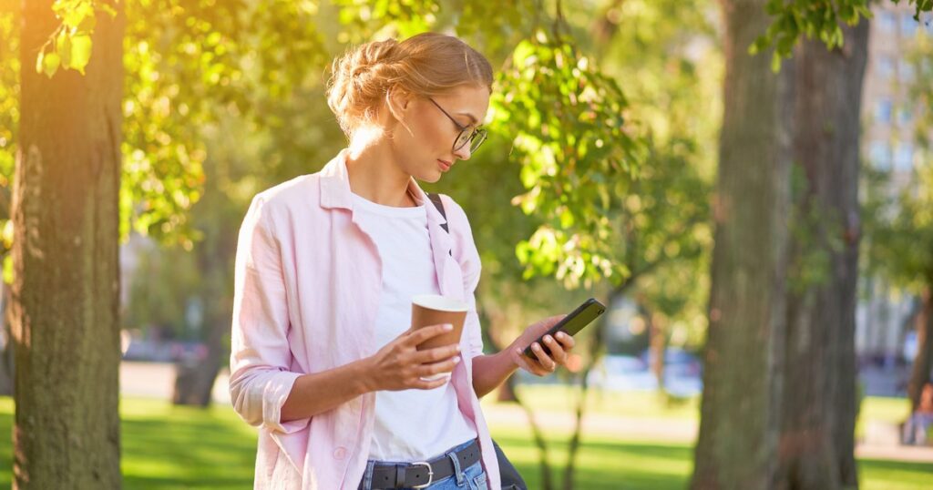 picture of woman outside holding cup and phone