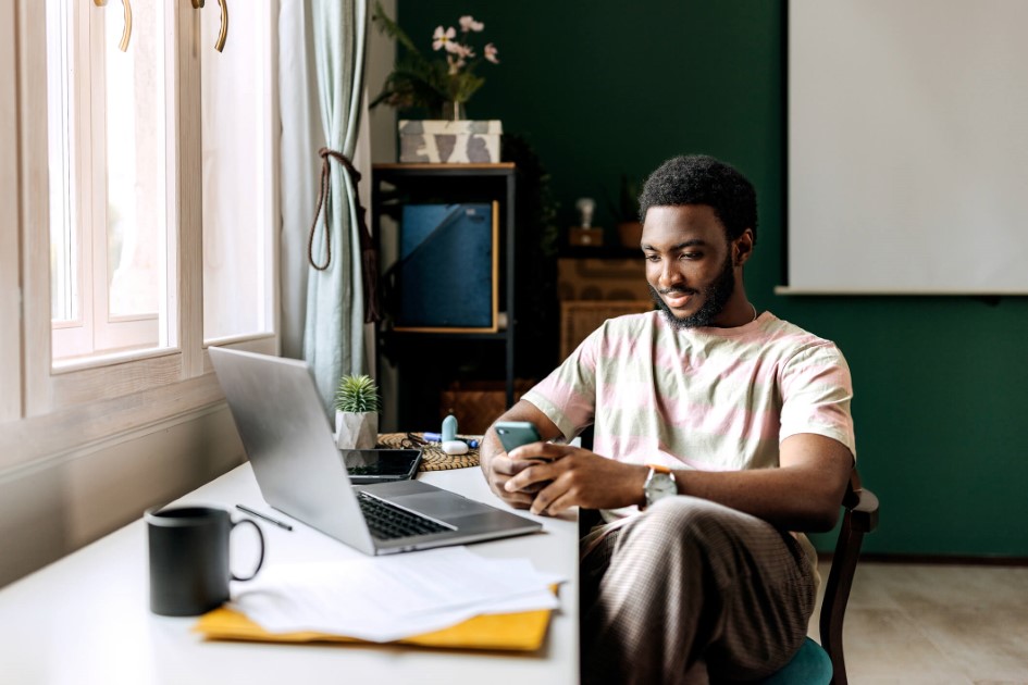 man sitting at computer while holding cell phone