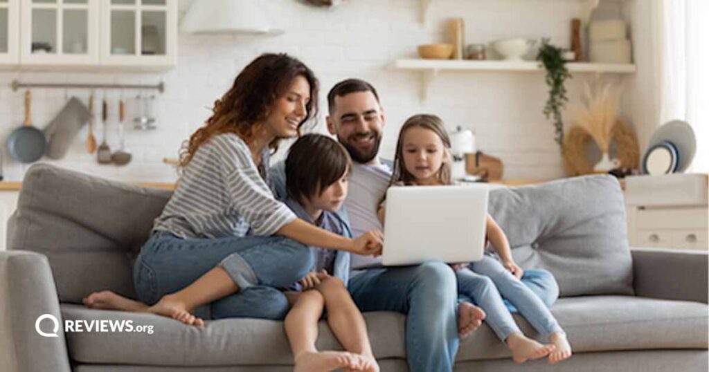 A mom, dad, and two children sit on a couch and use a laptop together