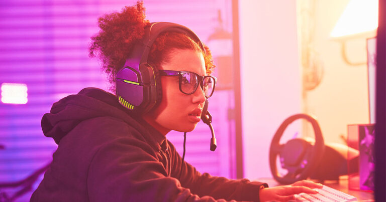 gamer wearing glasses and a headset on a pink hued backdrop