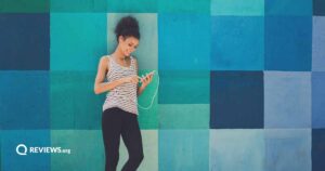 woman using cell phone and headphones standing against a blue checkered wall